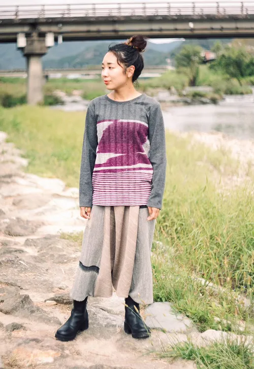 川辺で播州織の生地のトップスとサルエルバンツを着用した女性