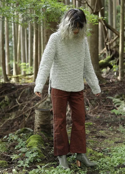 ワインカラーでアレンジワインダーの生地を使用したパンツを履いた女性が森の中で立っている