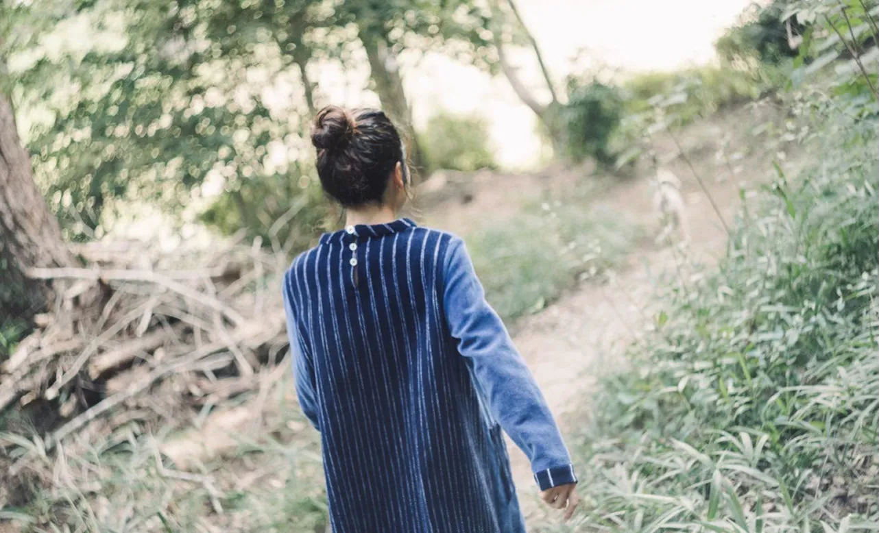 モール素材のワンピースを着た女の子が森の中を歩いている後ろ姿